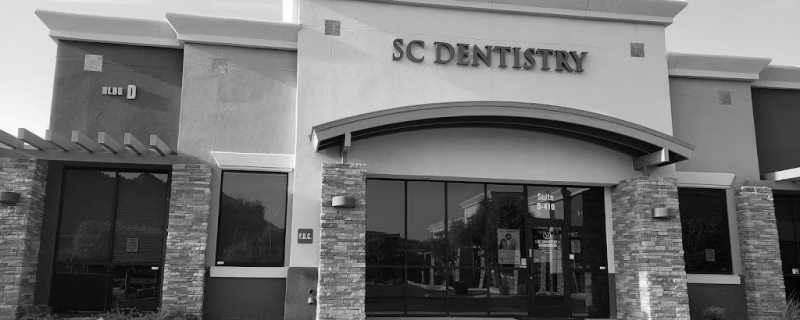 Exterior view of SC Dentistry office building featuring modern architecture with stone pillars, large glass windows and doors, arched entryway, and professional signage. Building labeled 